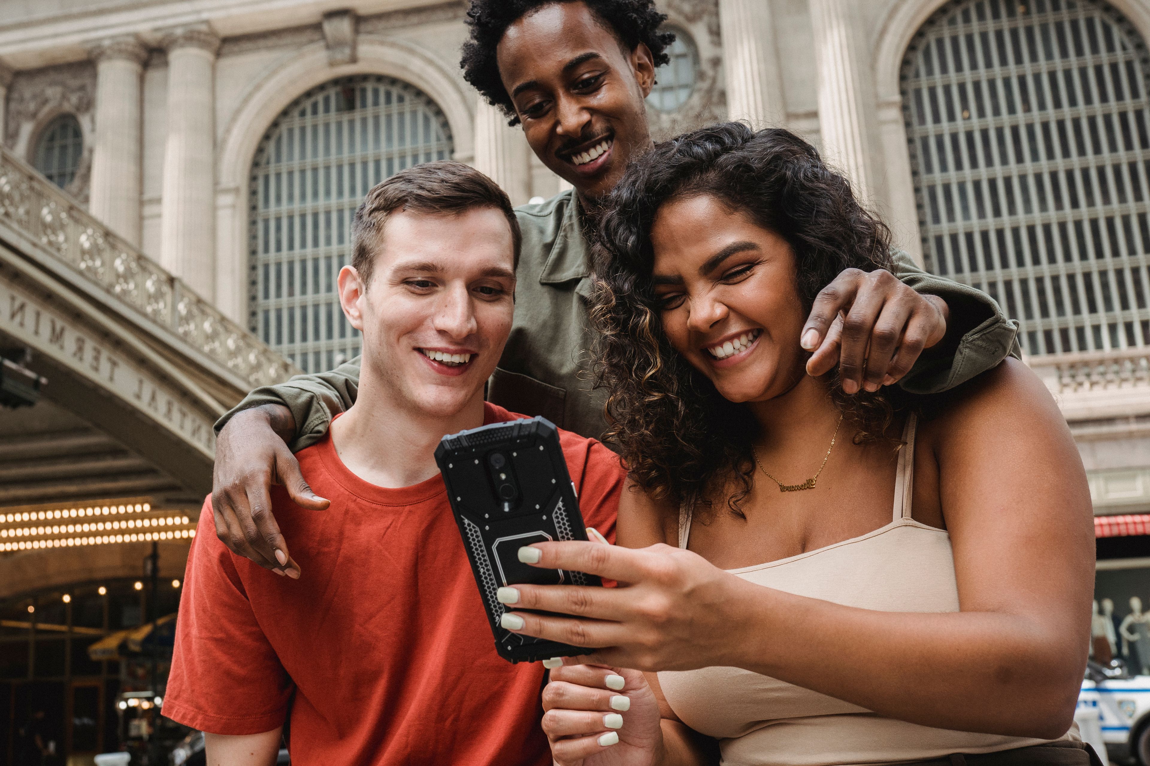 Three friends laughing together while looking at a phone
